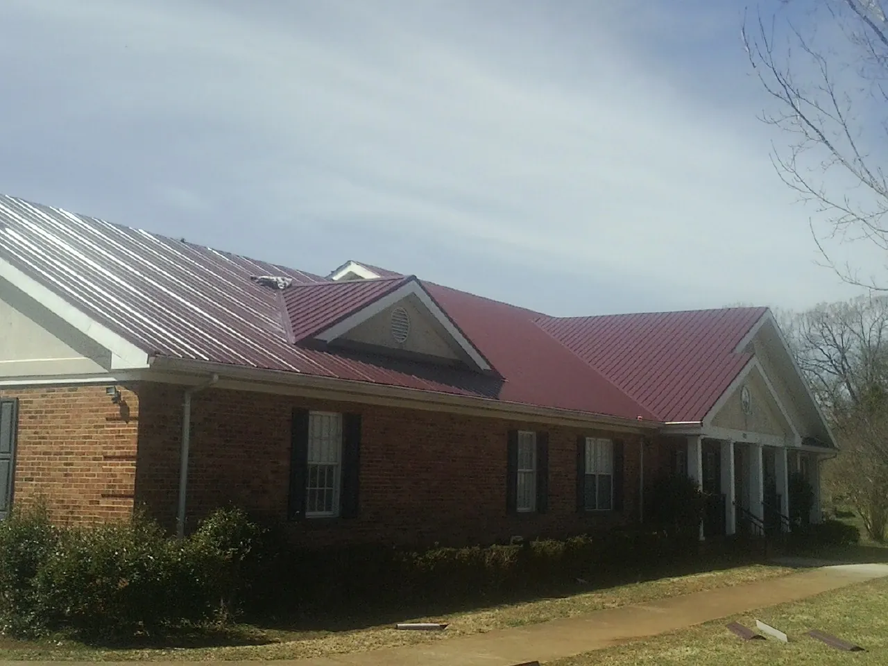 Red metal roof with gabled entries on a long brick building, from a Hail Damage Roof Repair job in Williamsport