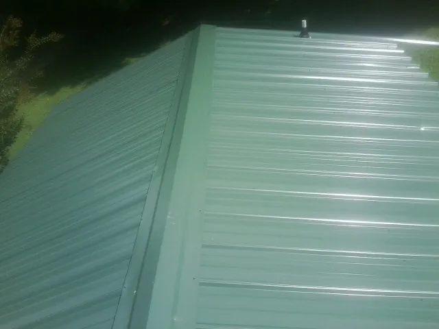 New green metal panels meeting at the ridge of a roof — Flat Roof Repair work by our crew in Williamsport