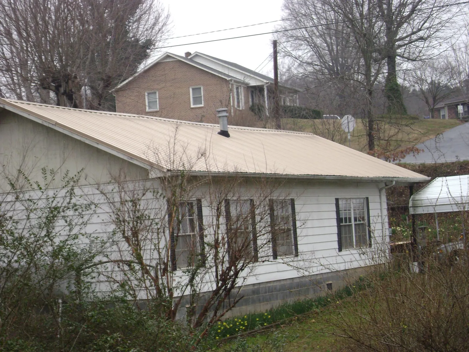 Tan metal roof on a white sided house set into a hillside — Commercial Roofing by Roofing Brothers in Williamsport
